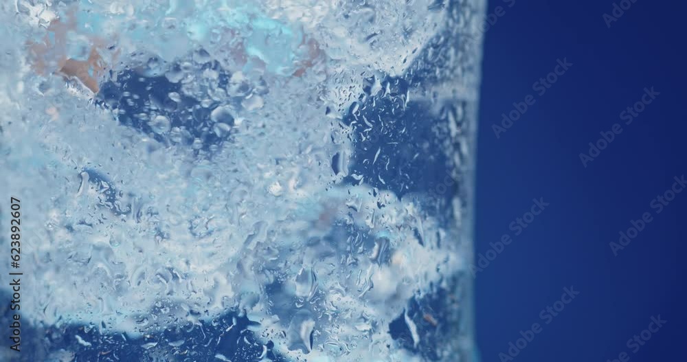 Ice cubes rotating in a glass with crystal clear water on a blue background. Refreshing and healthy water on hot days.