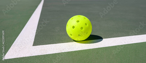 Closeup of a pickleball (whiffleball) on a sports court with white lines. © justasc