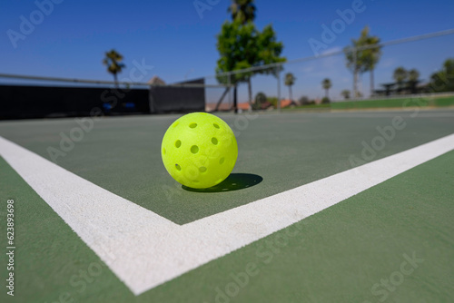 Closeup of a pickleball (whiffleball) on a sports court with white lines.