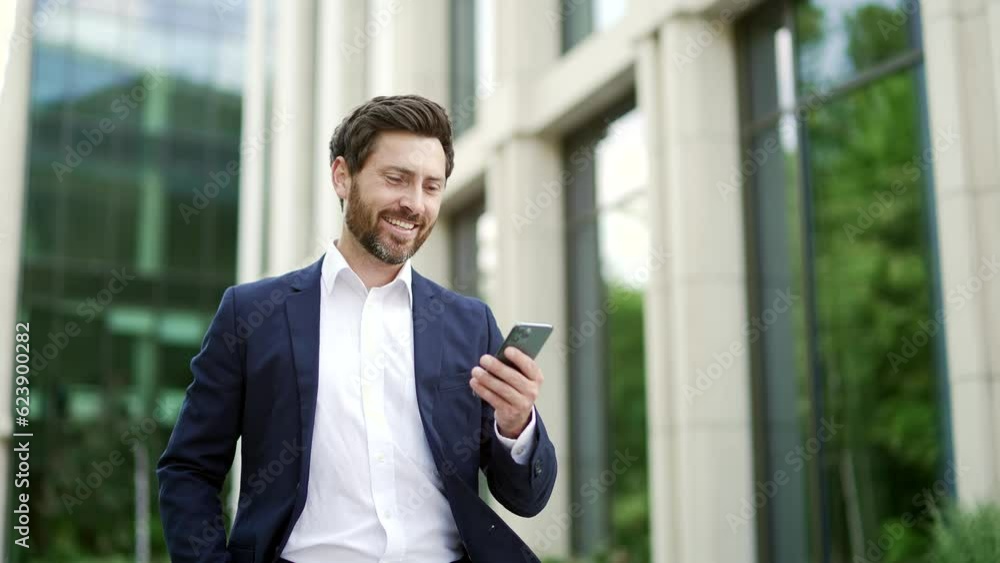 Confident mature bearded businessman in suit walking near modern business office building holding smartphone in hands. Man entrepreneur, investor, seo or manager using read a mobile phone outside Confident mature bearded businessman in suit walking near modern business office building holding smartphone in hands. Man entrepreneur, investor, seo or manager using read a mobile phone outside
