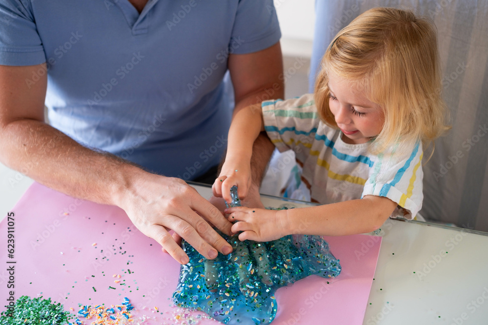 Smiling baby girl playing with bright slime with man, having fun indoors.Happy parenthood, father and daughter spending time together, happy childhood, creative games. Smiling baby girl playing with bright slime with man, having fun indoors.Happy parenthood, father and daughter spending time together, happy childhood, creative games.