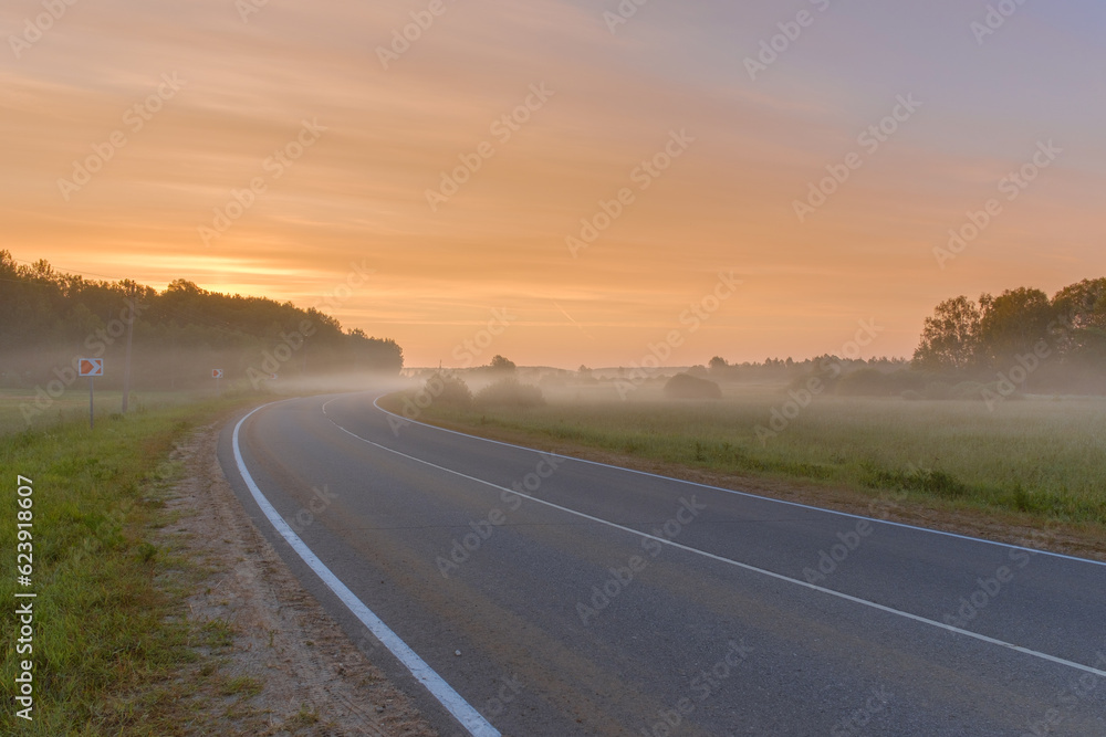 The asphalt road goes into the distance on a foggy summer morning. Beautiful foggy landscape.