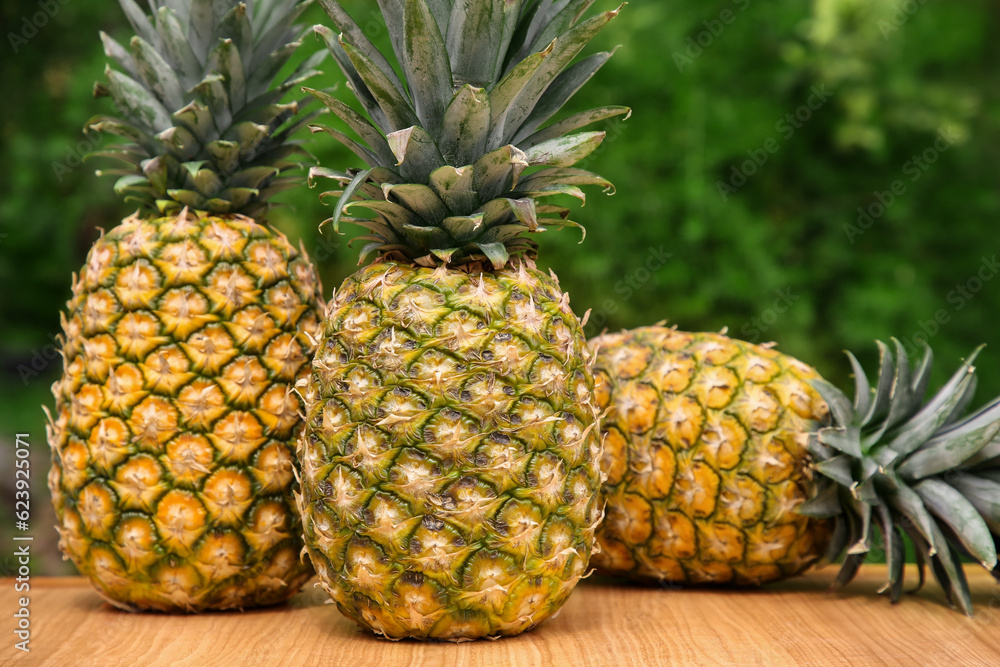 Delicious ripe pineapples on wooden table outdoors