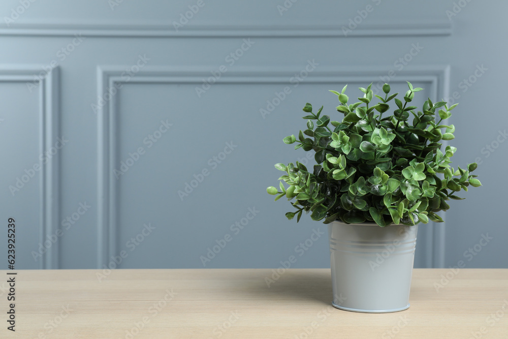 Beautiful artificial plant in flower pot on wooden table near grey wall, space for text Beautiful artificial plant in flower pot on wooden table near grey wall, space for text