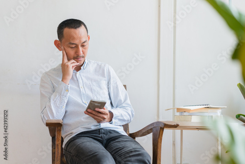 Young business man using mobile phone sitting at the chair in a home .