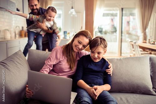 Young family spending time together at home and using a laptop on the couch