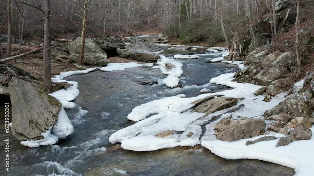 Slow motion close downstream flyover of winter stream with snow and ice. Slow motion close downstream flyover of winter stream with snow and ice.