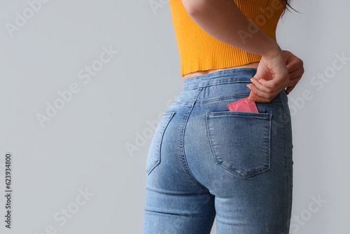 Young woman with condom in pocket on light background, back view