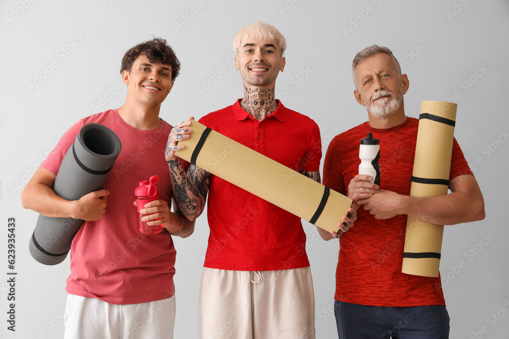 Sporty men with fitness mats and bottles of water on light background Sporty men with fitness mats and bottles of water on light background