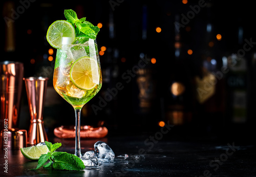 Hugo spritz alcoholic cocktail drink with dry sparkling wine or prosecco, elderflower syrup, soda, lime, mint and ice, dark bar counter background