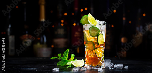 Fototapeta Naklejka Na Ścianę i Meble -  Pimms with cucumber, lime and ice - alcoholic cocktail drink with vodka, ginger beer and lemon juice, dark bar counter background, copy space.