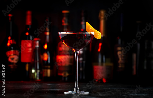 Adonis alcoholic cocktail drink with sherry and red vermouth, black bar counter background, steel tools and bottles photo