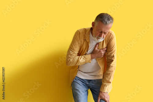 Mature man having heart attack on yellow background