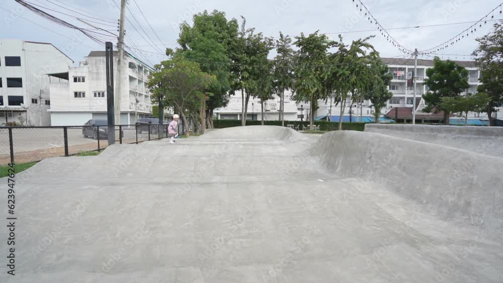 asian child skater or kid girl playing skateboard or ride surf skate and fun in pump track or wave bank to surfing in skatepark by extreme sports to wears helmet knee guard for body safety on slow asian child skater or kid girl playing skateboard or ride surf skate and fun in pump track or wave bank to surfing in skatepark by extreme sports to wears helmet knee guard for body safety on slow