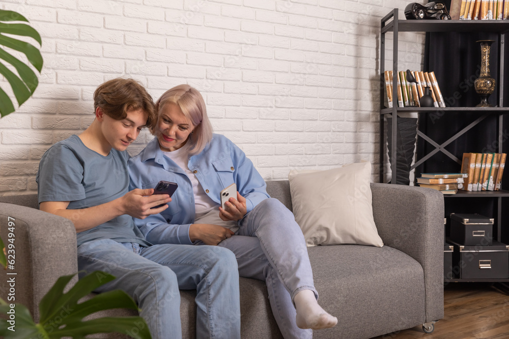 Photo of modern family relationships. Mom and teenage son look at their phones at home while sitting on the sofa