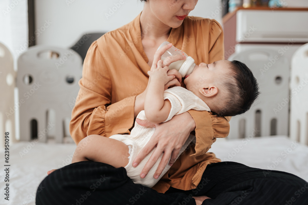Adorable little Asian baby sleep during drinking milk from baby bottle. Asian mother holding adorable her son and feeding milk from milk bottle. Concept babies healthcare. Adorable little Asian baby sleep during drinking milk from baby bottle. Asian mother holding adorable her son and feeding milk from milk bottle. Concept babies healthcare.