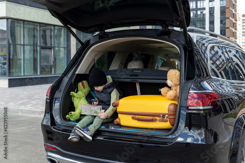 Cute little boy sitting in a car trunk before going on vacations with parents. Kid looking forward for a road trip or travel. Autumn break at school. Family travel by car.