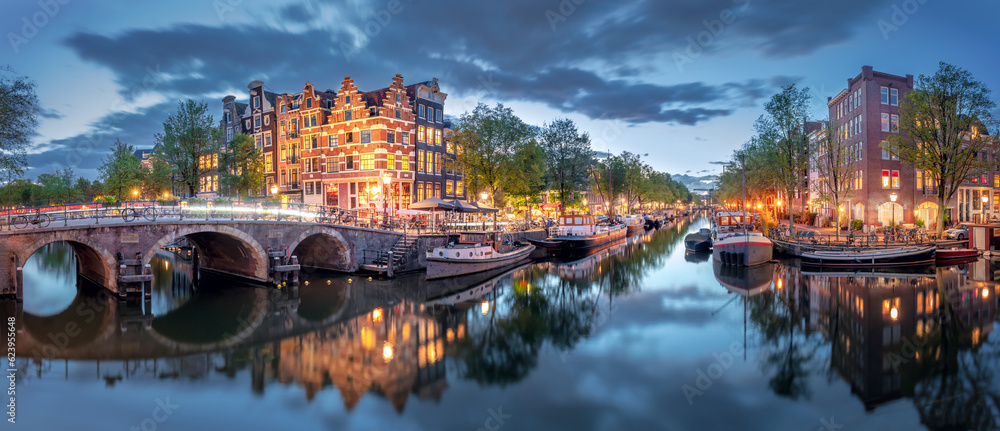 Amsterdam. Panoramic view of the historic city center of Amsterdam. Traditional houses and bridges of Amsterdam. A blue evening time and the serene reflection of lights in the water. Long exposure. Eu