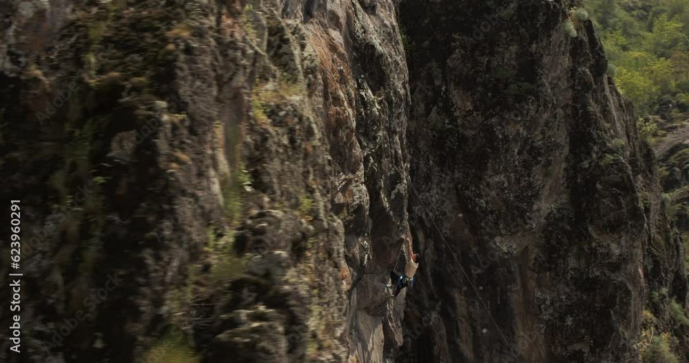A drone flies around a young athletic female climber hanging on one arm on a belay on a steep cliff A drone flies around a young athletic female climber hanging on one arm on a belay on a steep cliff