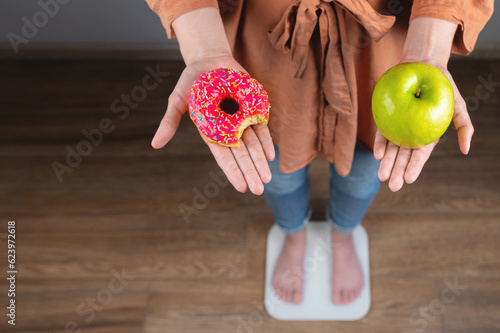 It's hard to choose a healthy food concept when a woman holds a green apple and a donut with a high-calorie dessert in her hand