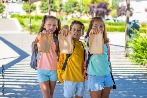 Group Of Classmates Smiling And Happy On The First Day Of School Carry Lunch For Break. Back To School © Nanci