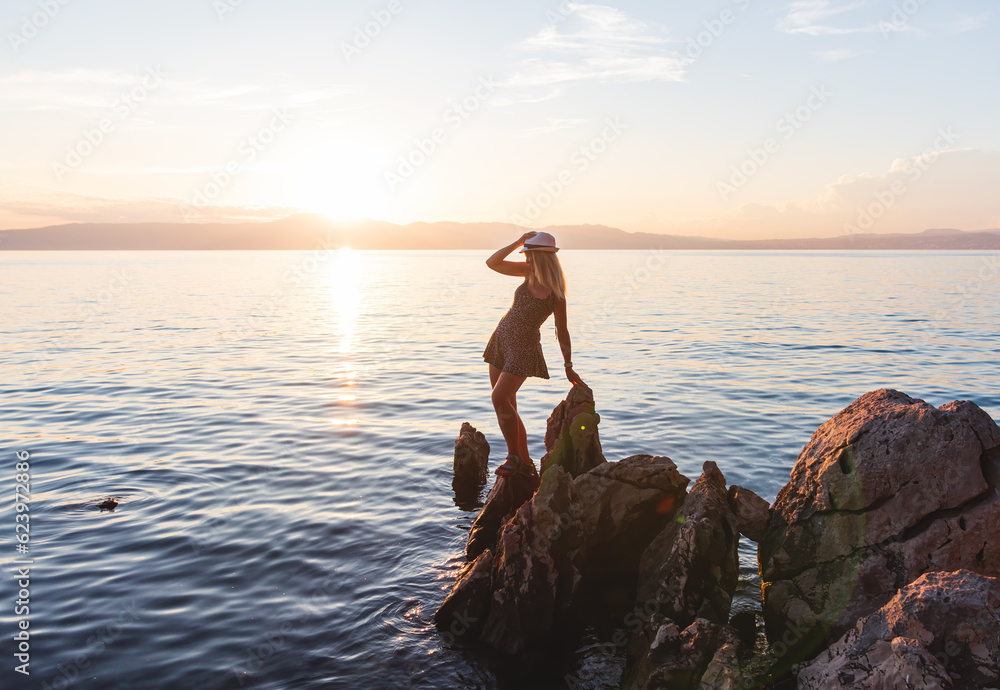 Beauty young woman in dress standing on rock in sea at sunset. Travel, nature background, Croatia