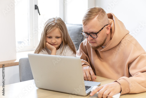 Father and daughter work at the computer. Dad explains something to his daughter. Information Technology. Internet. Classes online. Online learning.