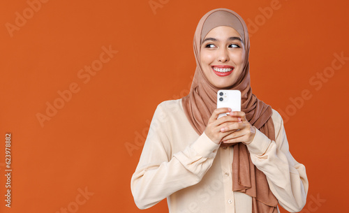 Beautiful overjoyed young smiling muslim woman in traditional religious hijab  reading great news on smartphone © JenkoAtaman