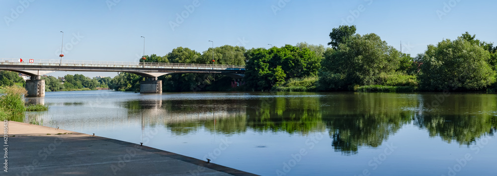 Panorama rzeki Odry w tle most lekko pochmurna pogoda, błękit nieba zieleń przy brzegu, pora letnia, Odra w odcinku województwa Opolskiego - obrazy, fototapety, plakaty 