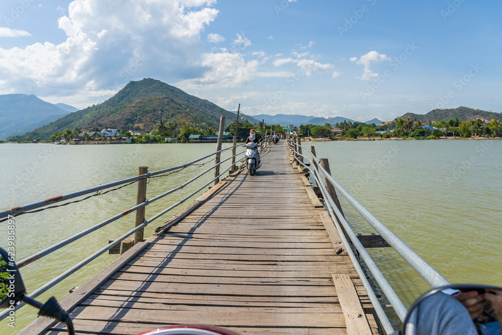 A motor scooter crossing a rustic wooden bridge towards a distant mountain
