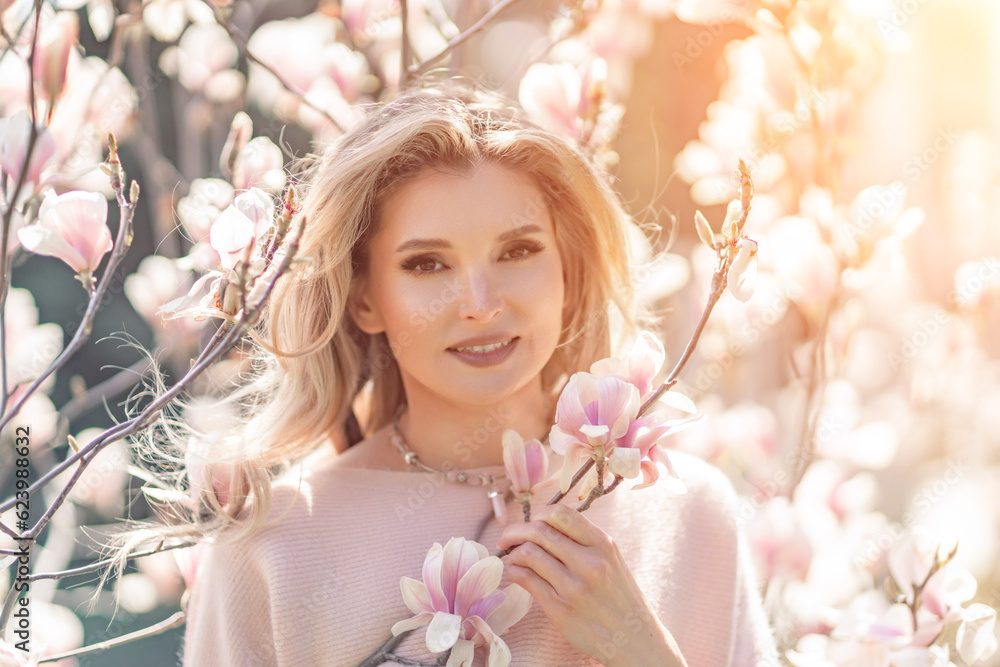 Fototapeta premium Magnolia woman portrait. Happy middle aged woman enjoying the smell in a blooming spring garden. Beautiful magnolia bushes, large flowers.