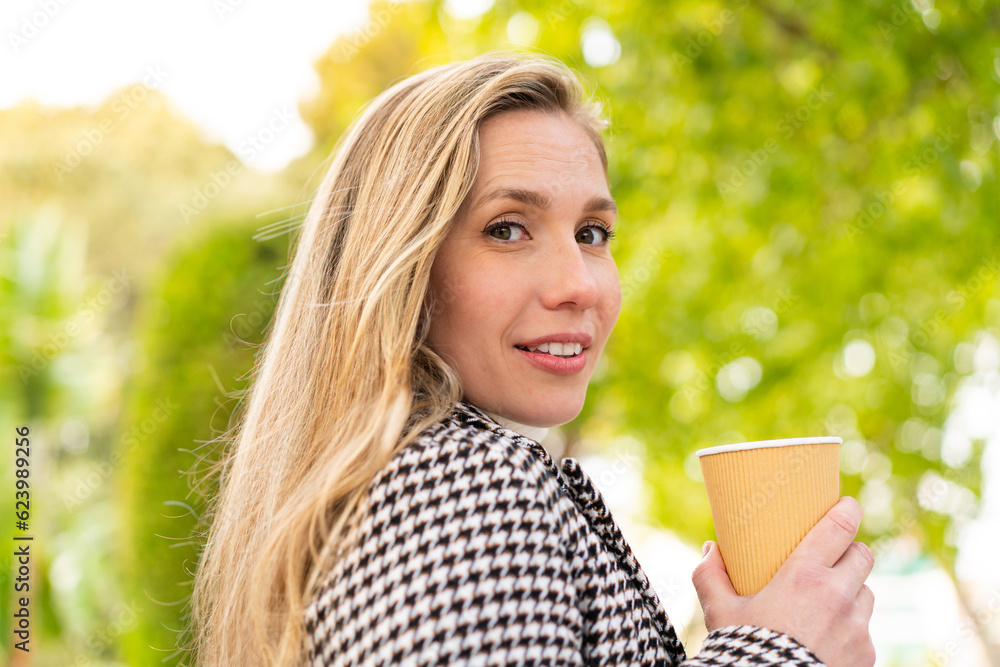 Young blonde woman holding a take away coffee at outdoors Young blonde woman holding a take away coffee at outdoors
