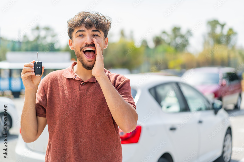 Fototapeta premium Young Arabian handsome man holding car key at outdoors shouting with mouth wide open