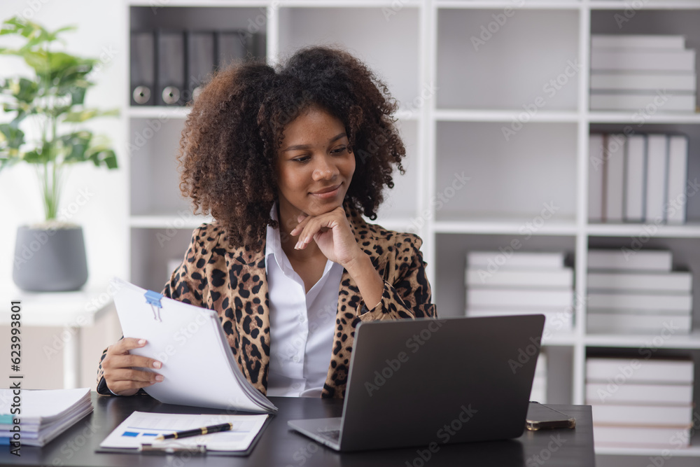 Young African American businesswoman working with smartphone and laptop at desk in office, business finance technology concept. Young African American businesswoman working with smartphone and laptop at desk in office, business finance technology concept.