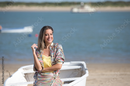 Pretty young blonde woman sitting in the fishermen's boats on the seashore. In the background on the horizon the blue sea and the boats working in the sea. Holiday and travel concept.