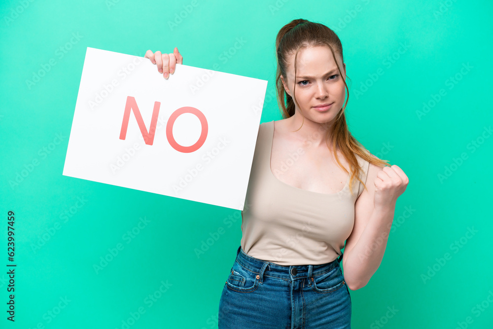 Young caucasian woman isolated on green background holding a placard with text NO and angry Young caucasian woman isolated on green background holding a placard with text NO and angry