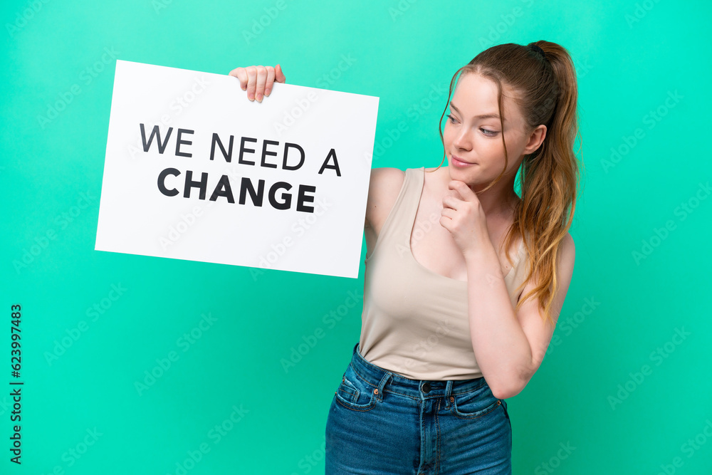 Young caucasian woman isolated on green background holding a placard with text We Need a Change and thinking Young caucasian woman isolated on green background holding a placard with text We Need a Change and thinking