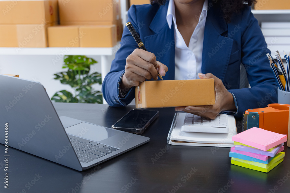 Happy African American businesswoman owner with a parcel box and checking orders from customers, online delivery service warehouse, sell products online concept. Happy African American businesswoman owner with a parcel box and checking orders from customers, online delivery service warehouse, sell products online concept.