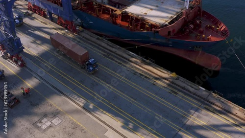 4K aerial footage over port. Drone following cargo trailers carrying containers unloaded from docked freight ship stock video. 