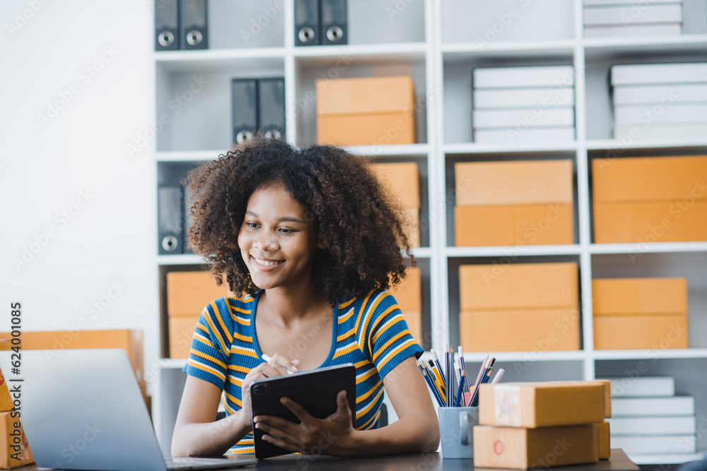 African American owner checking orders from customers sitting at desk in office, sell products online concept. African American owner checking orders from customers sitting at desk in office, sell products online concept.