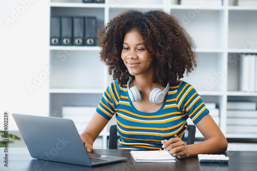 Young African American woman with wearing headphones and laptop at desk in office, Online education, Young African American.