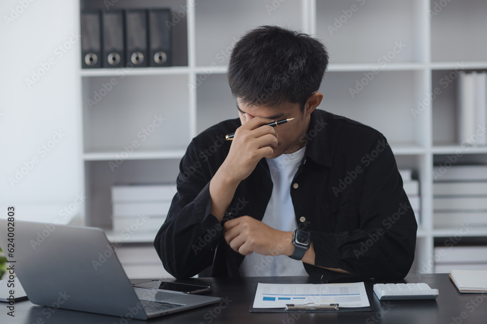 Asian businessman working online with laptop are stressed and tired from work sitting at desk in the office, feeling sick at work, stress from work. Asian businessman working online with laptop are stressed and tired from work sitting at desk in the office, feeling sick at work, stress from work.