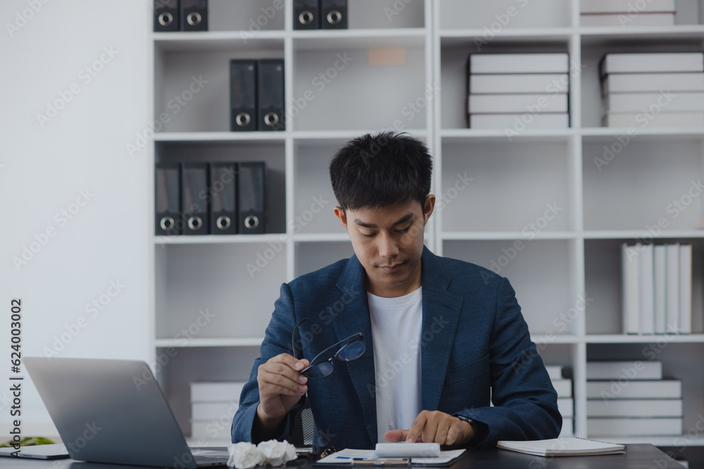 Asian businessman working online with laptop are stressed and tired from work sitting at desk in the office, feeling sick at work, stress from work. Asian businessman working online with laptop are stressed and tired from work sitting at desk in the office, feeling sick at work, stress from work.