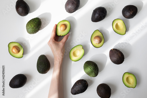 Konstfotografi Woman hand holding half avocado of heap whole avocados on table top view in aesthetic shadow sunlight