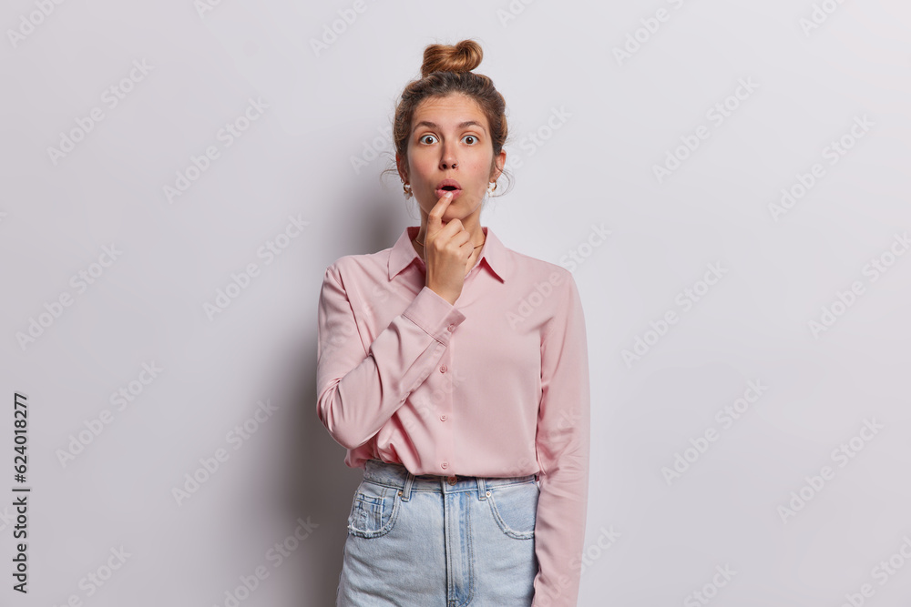 Studio waist up of young beautiful fit European female surprised seeing something unusual standing in centre on white background wearing casual clothes keeping hair in bun. People emotions concept. Studio waist up of young beautiful fit European female surprised seeing something unusual standing in centre on white background wearing casual clothes keeping hair in bun. People emotions concept.