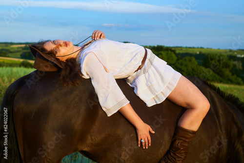 Beautiful girl laying on a horse on the sunset