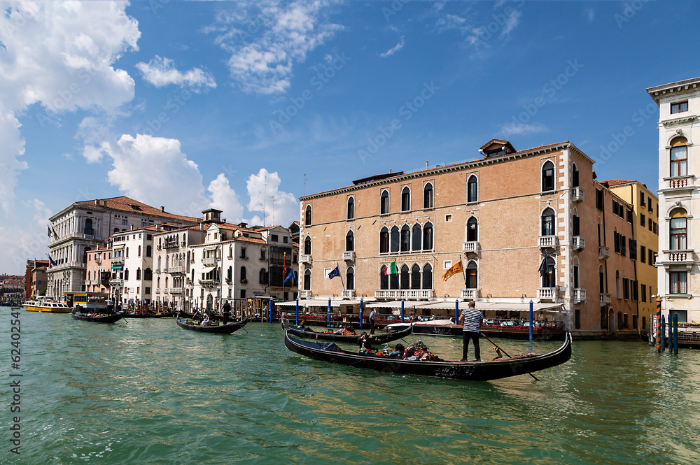 View of the Grand Canal with gondolas with tourists and the  palazzo Pisani-Gritti building on the shore of canal on a sunny summer day. Venice, Italy