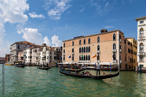 View of the Grand Canal with gondolas with tourists and the palazzo Pisani-Gritti building on the shore of canal on a sunny summer day. Venice, Italy