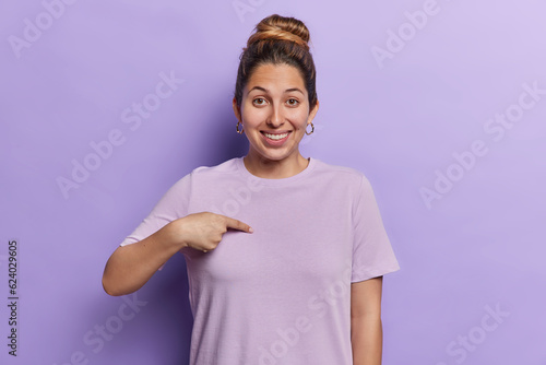 Fotografija Waist up shot of cheerful beautiful European woman points at herself asks who me smiles pleasantly glad to be chosen dressed in casual t shirt isolated over purple background