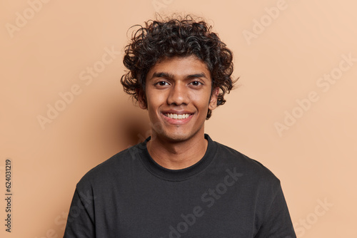 Wallpaper Mural Portrait of handsome cheerful man with curly hair smiles toothily poses happy against brown background dressed casually isolated over brown background